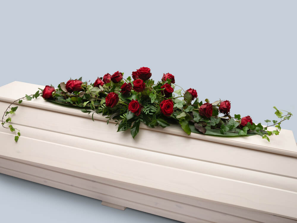 Näyttävä iso punaisista ruusuista ja muratista tehty arkkulaite, jossa muratinoksat ulottuvat arkun pituudelta. Hautauspalvelu Kaiho Oy - Hautajaiskukat kuva