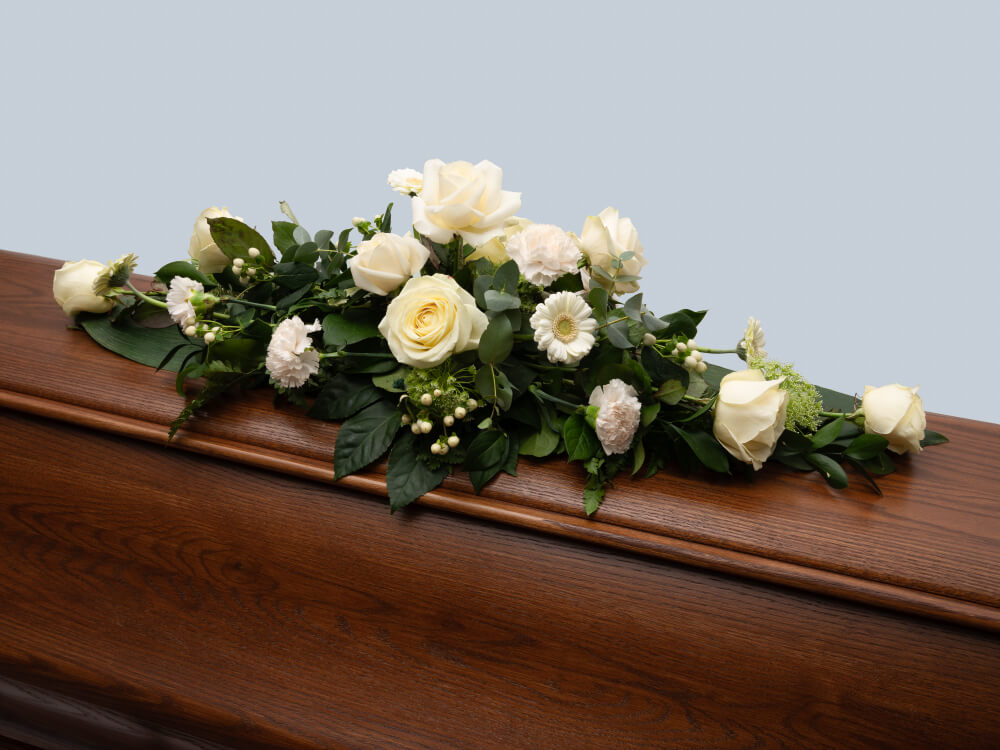Arkkulaitteessa on valkoisia ruusuja, germiinejä ja neilikoita, valkoista marjakukkaa, vihreitä lehtiä. Hautauspalvelu Kaiho Oy - Hautajaiskukat kuva