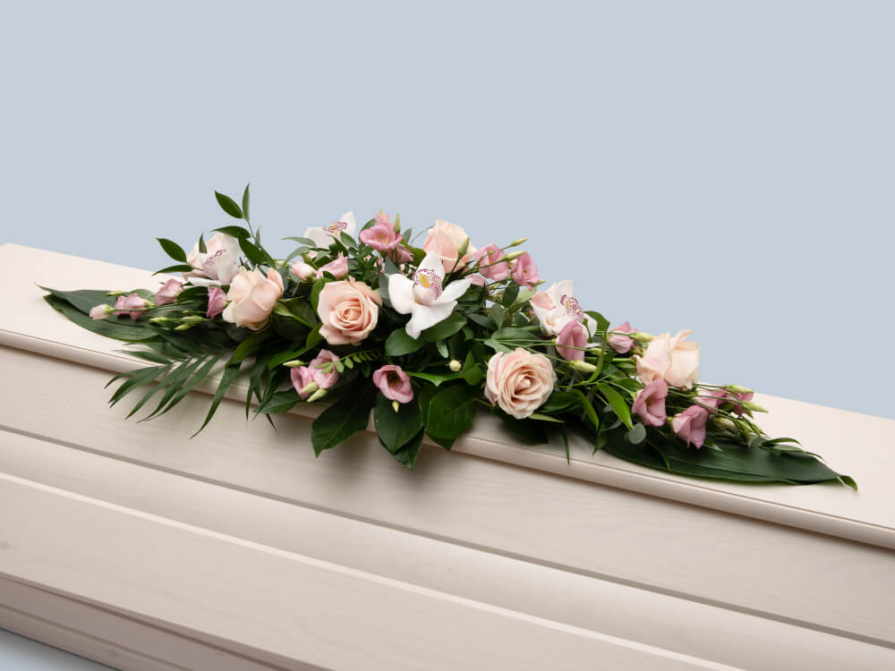 Leveä, kaunis vaaleanpunakukkainen sidonta valkoisen arkun päällä, Hautauspalvelu Kaiho Oy - Hautajaiskukat kuva