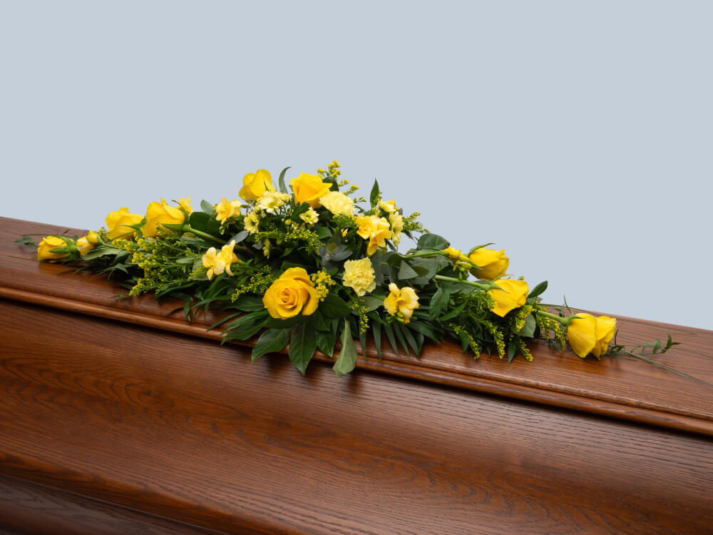 Arkkulaitteessa on keltaisia ruusuja ja neilikoita. Hautauspalvelu Kaiho Oy - Hautajaiskukat kuva