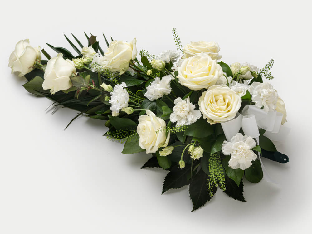 Pisaranmuotoinen surulaite, jossa valkoisia ruusuja neilikoita, pieni valkoinen rusetti vihreän kahvan luona. Hautauspalvelu Kaiho Oy - Hautajaiskukat kuva