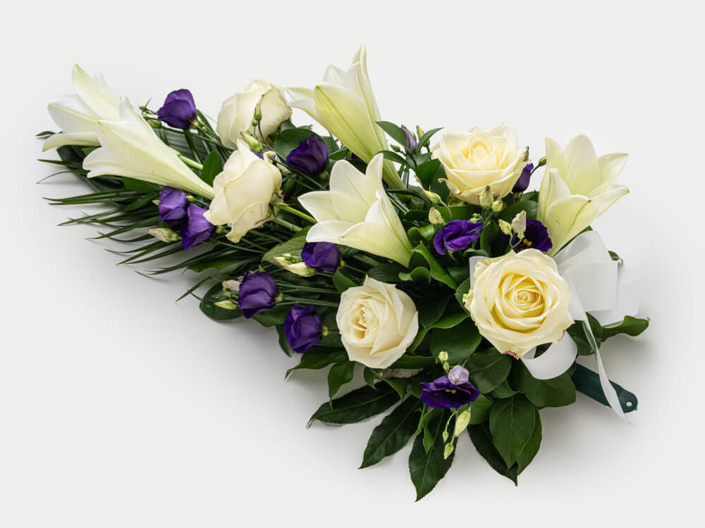 Valkoisia liljoja ja ruusuja, violettia eustomaa joukossa, valkoinen rusetti ja vihreä kahva. Hautauspalvelu Kaiho Oy - Hautajaiskukat kuva