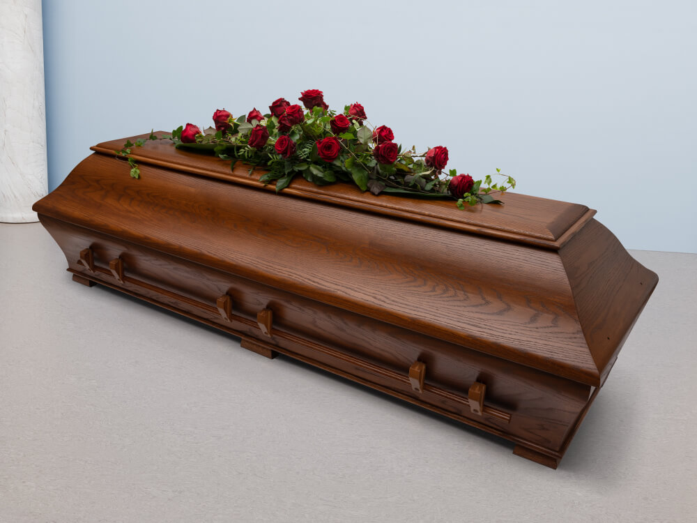 Tummanruskea jyhkeä arkku, kansi muodoltaan kaareva, pitkä yhtenäinen tanko kahvoina. Arkun päällä tummanpunaisista ruusuista tehty komea arkkulaite.