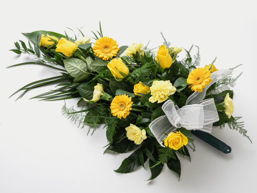 Keltaisia ruusuja ja gerberoita sekä vaaleankeltaisia neilikoita, runsaasti vihreää. Hautauspalvelu Kaiho Oy - Hautajaiskukat kuva